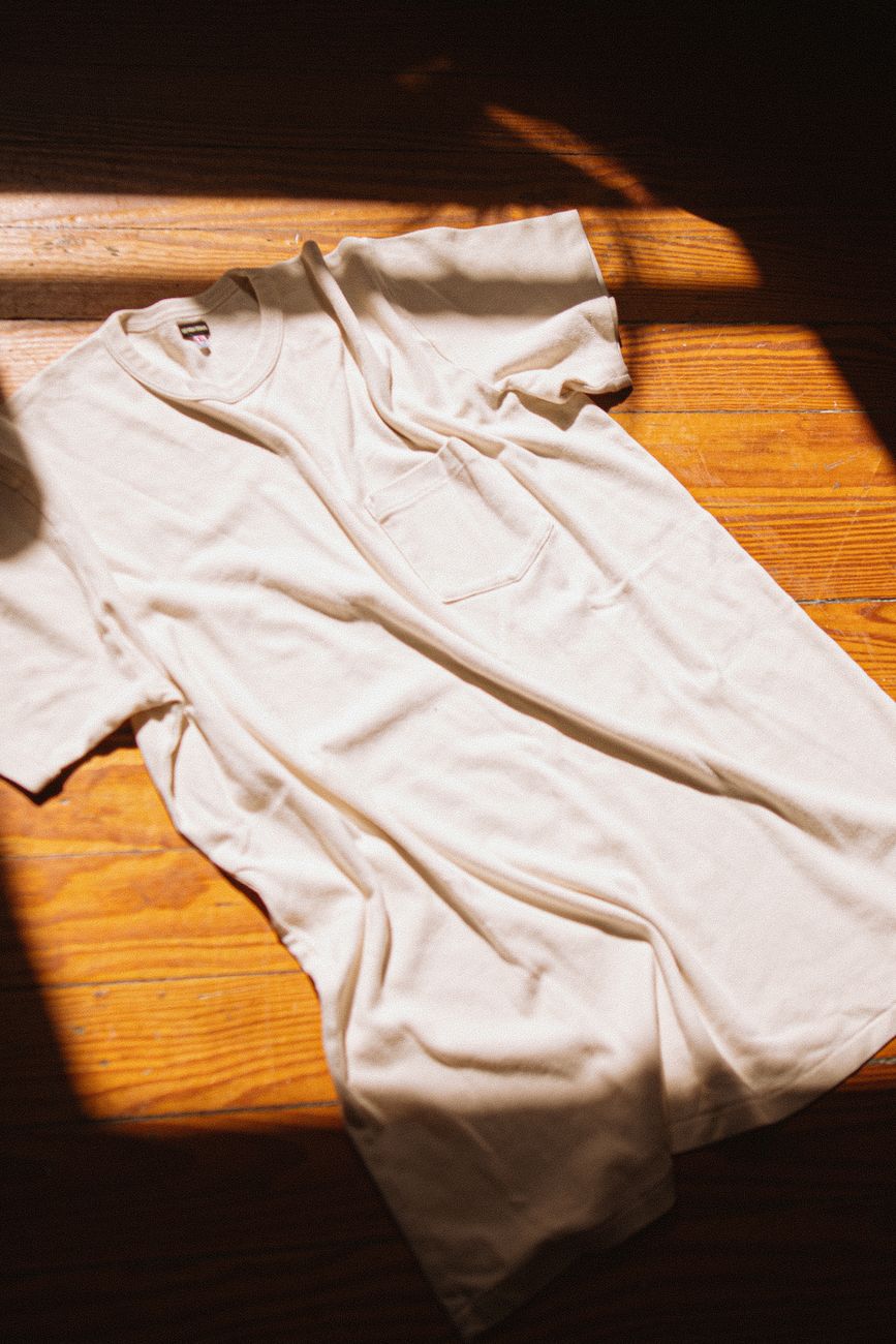 Remera blanca extendida sobre piso de madera con luz de sol